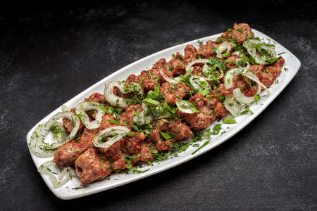 LULYA-KEBAB with herbs and onions on a plate, on a dark background
