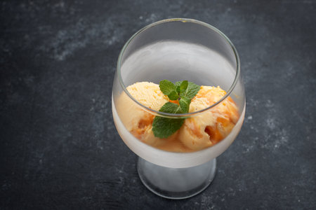Pumpkin ice cream in a glass goblet, on a black background with a wooden boardの写真素材