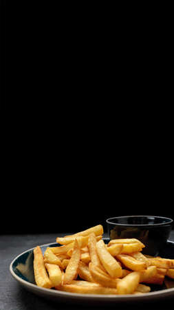 French fries with sauce on a plate, on a dark background