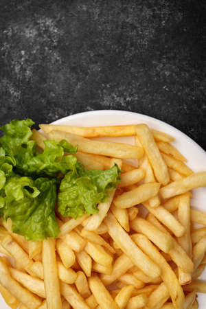 Fried potatoes with lettuce, on a plate, on a black backgroundの写真素材