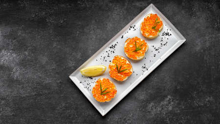 Bruschetta with red caviar on a plate with lemon and green onions
