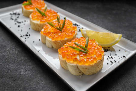 Bruschetta with red caviar on a plate with lemon and green onions