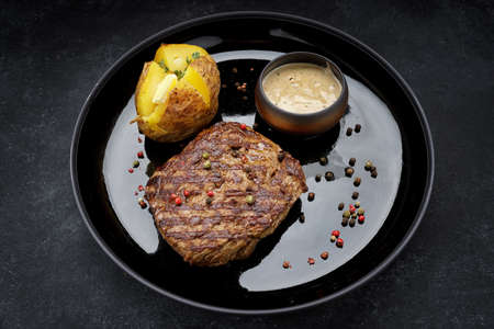 Grilled pork steak with baked potatoes, mustard sauce, pepper. On a plate, on a dark backgroundの写真素材
