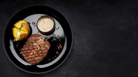 Grilled pork steak with baked potatoes, mustard sauce, pepper. On a plate, on a dark backgroundの写真素材