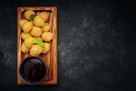 Cheese nuggets balls with sweet sauce on a wooden board, on a dark backgroundの写真素材