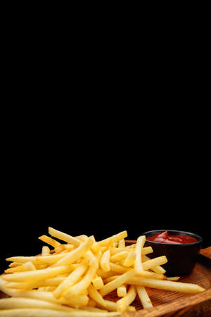 French fries with sauce on a wooden board, on a black background