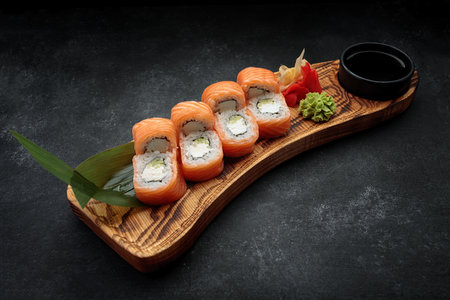 Sushi roll Philadelphia, with wasabi and ginger, on a wooden board with a leaf of bamboo, on a dark backgroundの写真素材