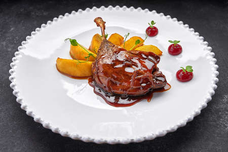 Duck leg with pear in caramel, on a white plate, on a dark backgroundの写真素材