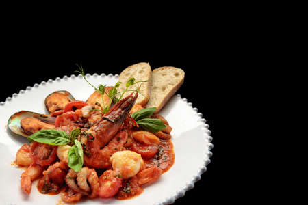 Sauteed seafood with shrimps, mussels, squid and scallop on a white plate, on a dark background