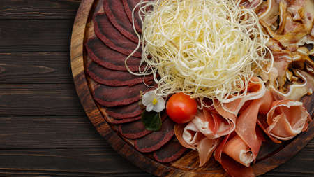 Set of snacks for beer, dried squid, basturma, jamon, pork ears and cherry tomatoes, on a plank wooden backgroundの写真素材