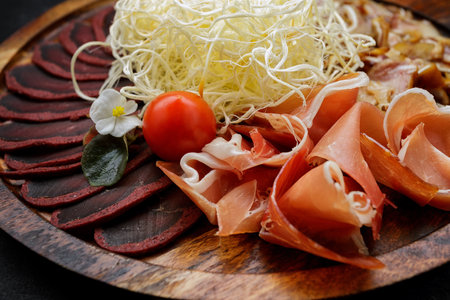 Set of snacks for beer, dried squid, basturma, jamon, pork ears and cherry tomatoes, on a dark backgroundの写真素材