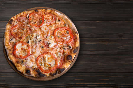 Pizza with mushrooms and tomatoes, on a round wooden board, on a wooden backgroundの写真素材
