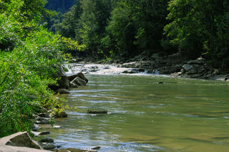 Mountain river with rapids and large stones on a sunny day