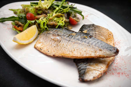 Two baked mackerel fillets on a plate, with thyme, rosemary and lemonの写真素材