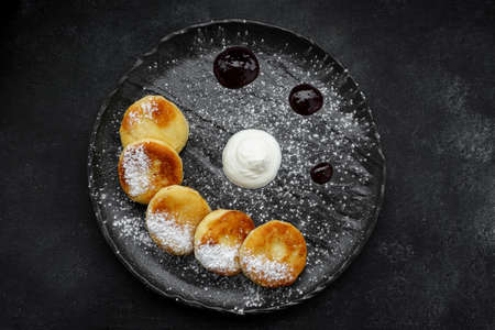 Cottage cheese cheesecakes on a black plate with sour cream