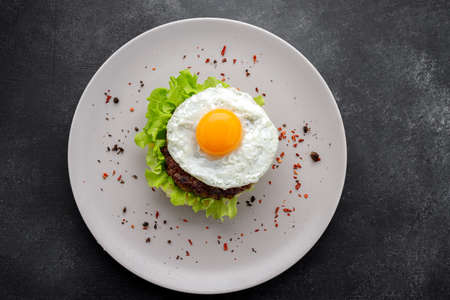 Beefsteak with egg, lettuce, spices and mashed potatoes on a dark background