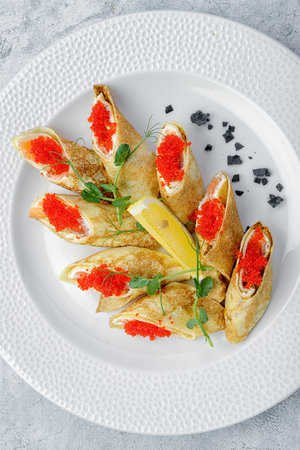 Pancakes with salmon, cream cheese and Tobiko. on a white plate