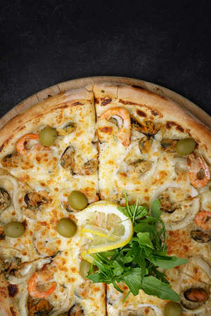 Marinara pizza with squid mussels shrimp olives and lemon, on a wooden round board on gray concrete.の写真素材