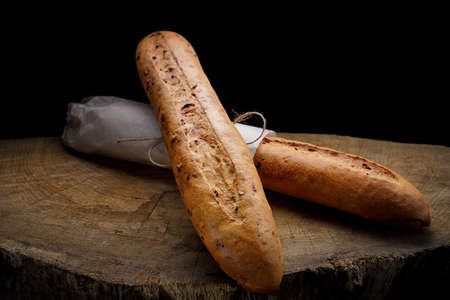 Two white baguette bread on a wooden board on a black backgroundの写真素材