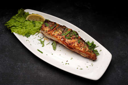 Grilled headless mackerel with herbs on a plate, on gray concrete