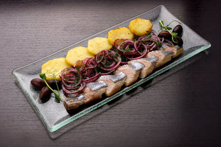 Sliced herring fillet with potatoes, onions and olives on a plate