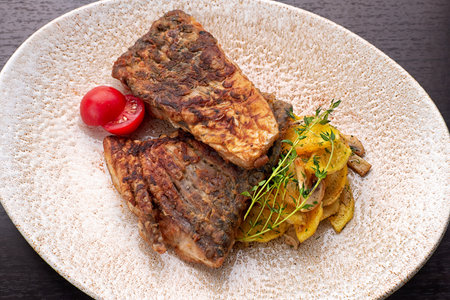 Pieces of fried fish with fried potatoes with mushrooms, tomatoes and herbs