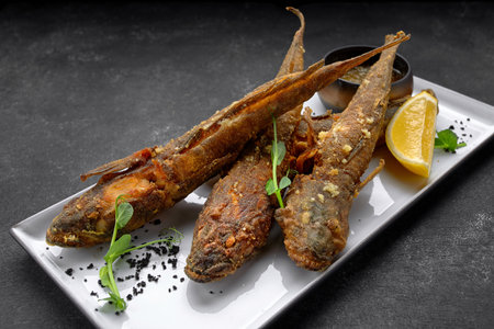 Fried Goby fish, with sauce and lemon, on a dark background