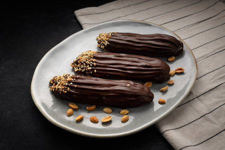 Eclairs with custard and nuts, on a dark background
