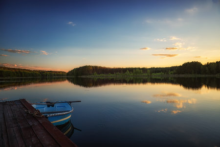 summer evening on the bank of a forest river, a place for fishing on a wooden bridge, and a boat, and a reflection in the waterの写真素材