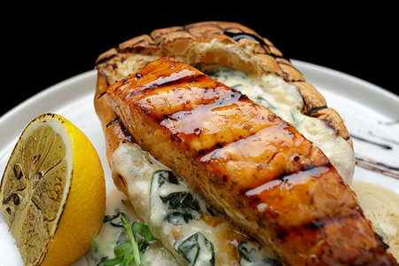 Grilled salmon fillet steak with sauce and ciabatta, on a black background