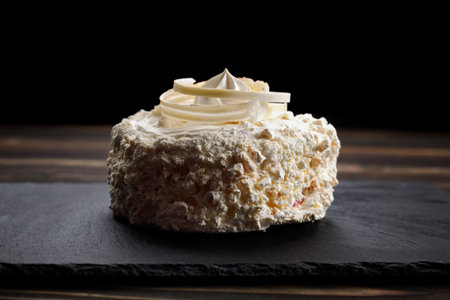 White dessert meringue with cream on a black stone, on a wooden background