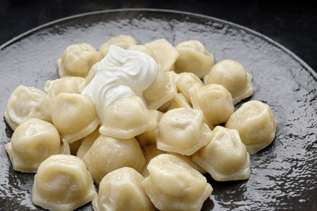 Ukrainian dumplings with sour cream, on a black glossy plateの写真素材