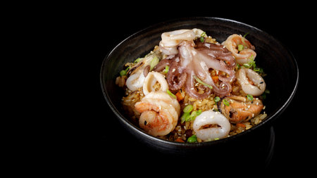 Spicy yellow rice with shrimps, octopus, mussels and vegetables close-up in a black bowl. horizontalの写真素材