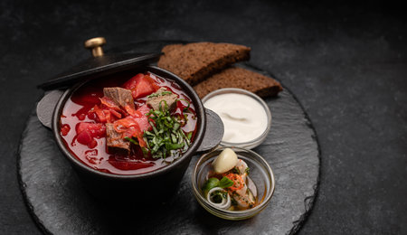 Red borscht with meat, sour cream and black bread, in a cauldron on a dark backgroundの写真素材