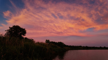 A peaceful and warm sunset over the calm lake, casting golden hues across the sky and reflecting on the waterの写真素材