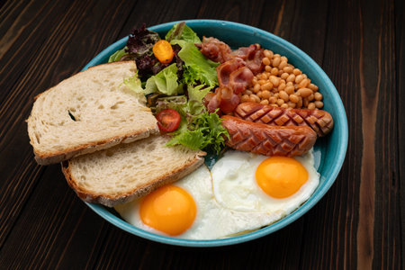 Close-up of a traditional English breakfast with eggs, bacon, sausages, beans, and toast on a plateの写真素材