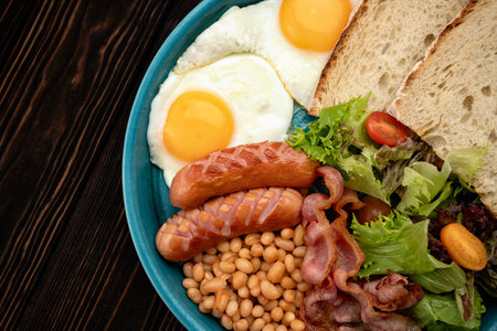 Close-up of a traditional English breakfast with eggs, bacon, sausages, beans, and toast on a plateの写真素材