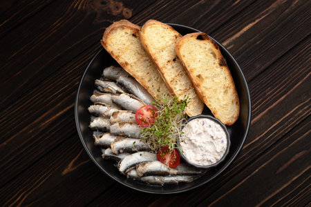 Close-up of sprats served with crispy bread toasts and creamy sauce on a black plate.の写真素材