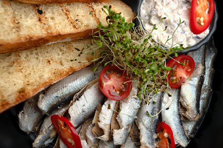 Close-up of sprats served with crispy bread toasts and creamy sauce on a black plate.の写真素材