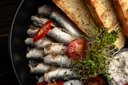 Close-up of sprats served with crispy bread toasts and creamy sauce on a black plate.の写真素材