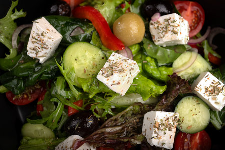 Fresh classic Greek salad with tomatoes, cucumbers, olives, and feta cheese, styled on a dark...