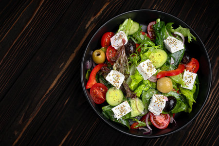 Fresh classic Greek salad with tomatoes, cucumbers, olives, and feta cheese, styled on a dark background for menu design and restaurant advertising.の写真素材
