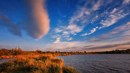 Scenic warm sunset on the lake shore with glowing sky and calm water reflecting vibrant colors. Peaceful and atmospheric nature landscape.の写真素材