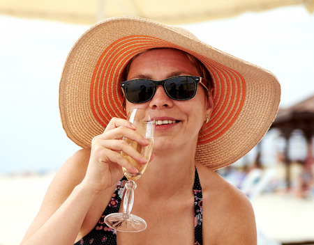 Beautiful girl in wide-brimmed hat drinking champagne at the beachの写真素材