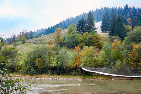 Mountain river with suspension hanging bridge in foggy rainy weatherの写真素材