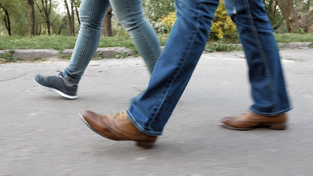 Women's feet on the sidewalk in shoes and sneakers trainers and jeans. Closeup tracking shot.