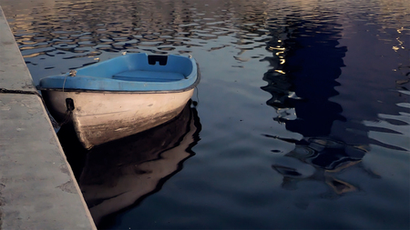 Boat at the quay moorage at sunset reflecting in water in the evening twilight dusk. Summer warm and calm concept.の写真素材