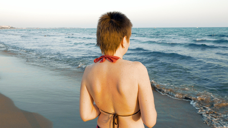 Woman in bikini watching sunset on beach. Enjoying summer vacation on tropical country on blue sea waves background. Relaxing evening walkの写真素材