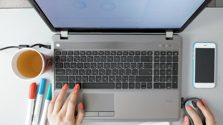 Female hands working on her laptop on graphic design. POV from first person. The smartphone paper cap and highlighters are shown on her desk. Modern computer technology has improved.の写真素材