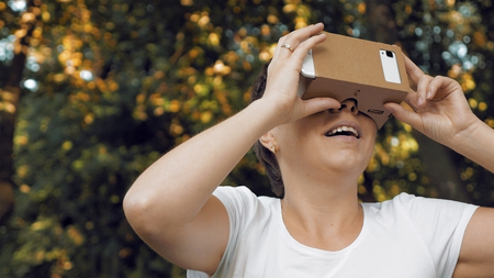 Woman explores virtual reality using cardboard VR glasses. Augmented reality quickly comes in human lives. VR mounted displays helmets and glasses are the most popular devices for playing AR games.の写真素材